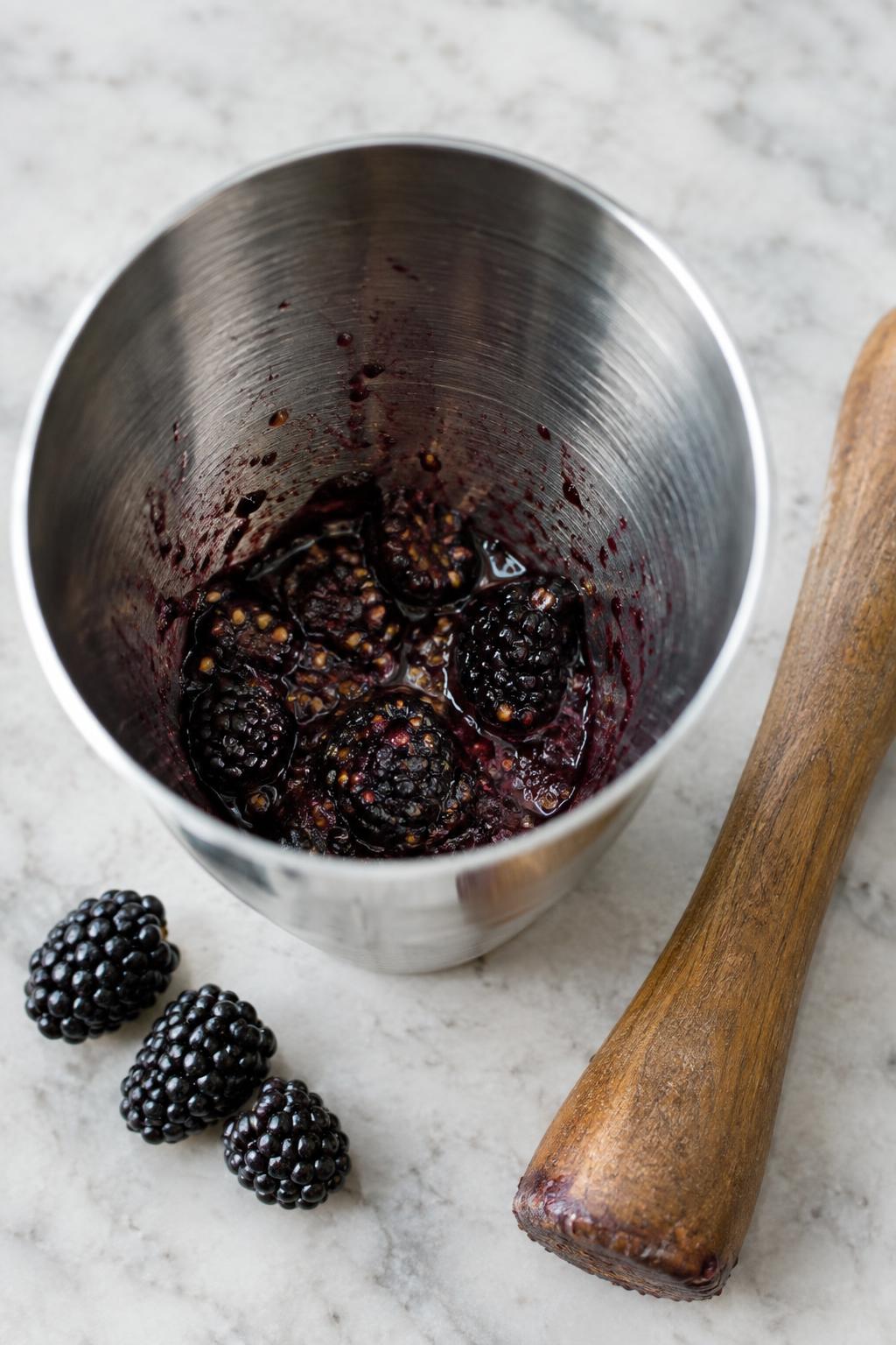three blackberries muddled at the bottom of a cocktail shaker
