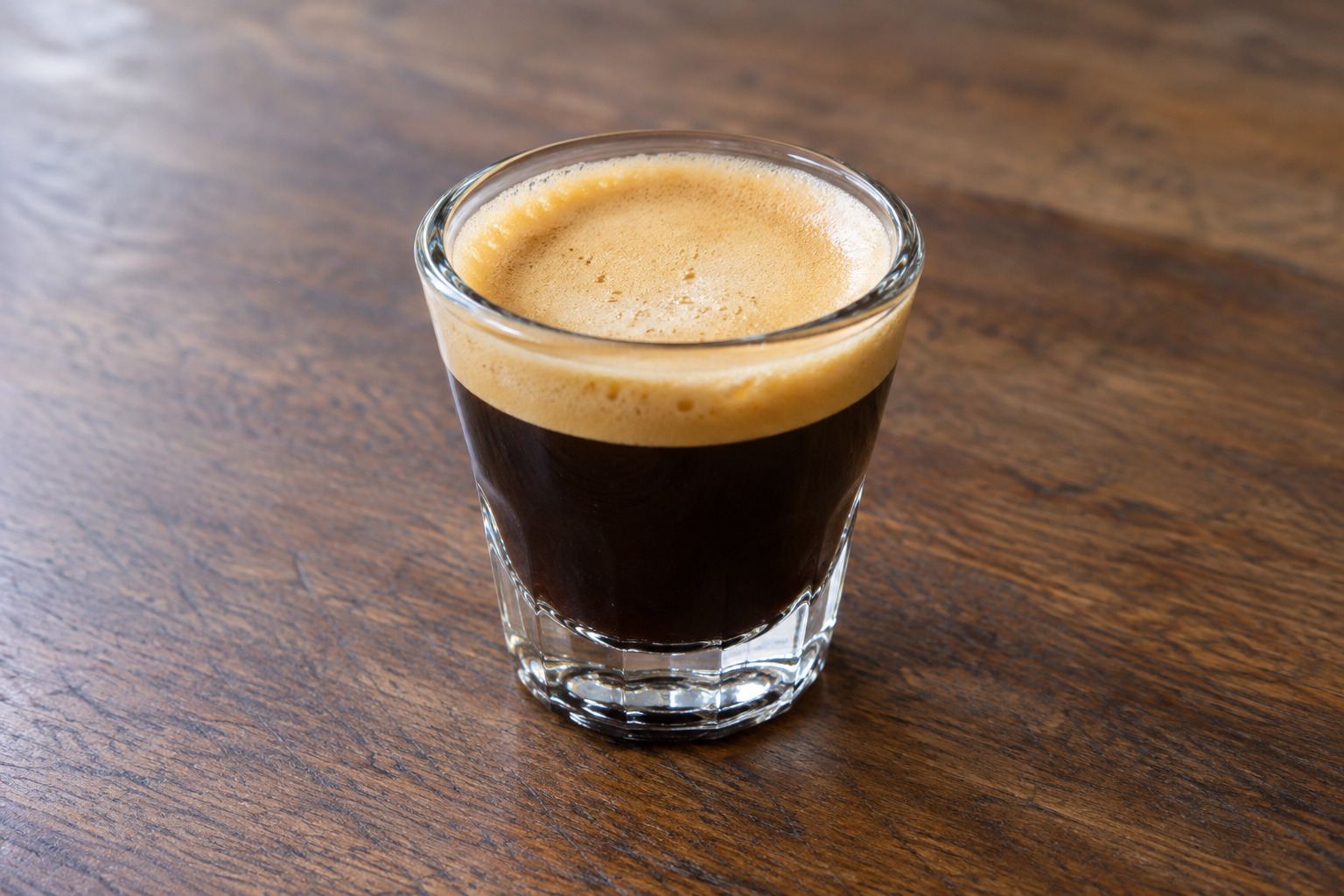 Spoon beating dark espresso and white sugar together in a small glass container, mixture turning pale and creamy
