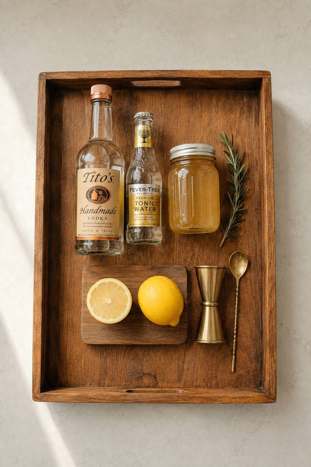 Overhead view of a small tray holding three bottles, a short cutting board with a halved lemon, and a jigger, showing how little counter space the whole setup needs